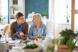 Healthcare worker with senior woman patient at her home, using a tablet and speaking