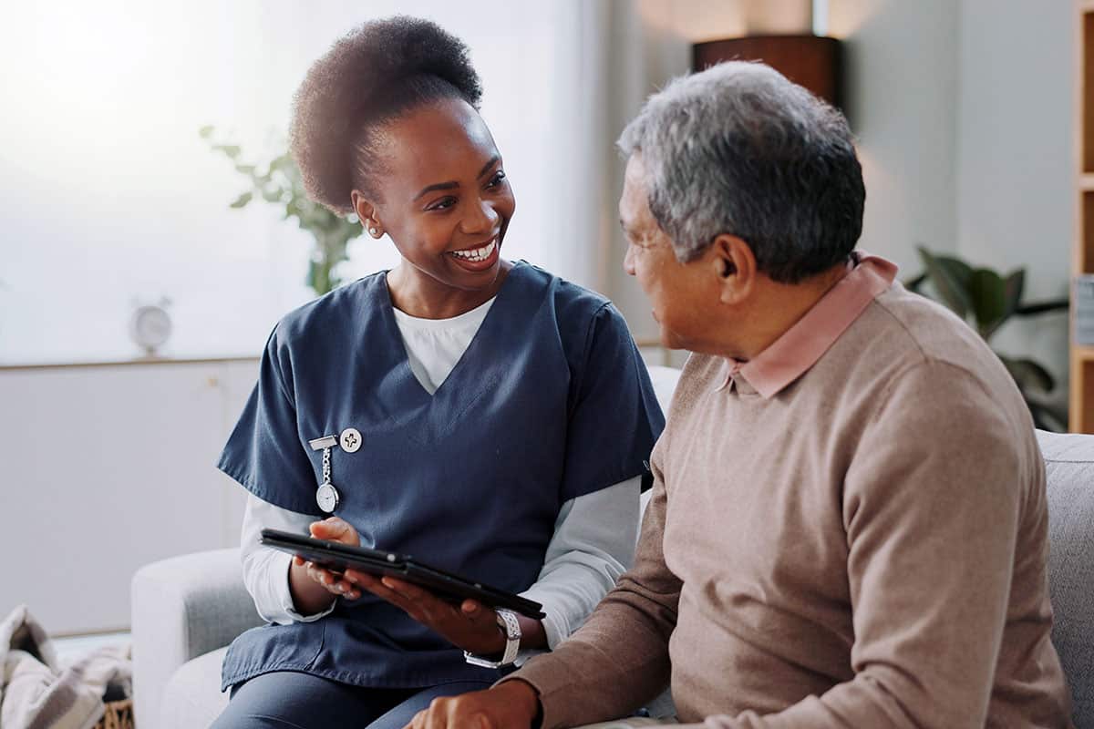 Home nurse sitting with client and smiling while holding a tablet