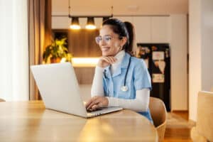Home care nurse sitting at kitchen table and smiling while looking at a laptop