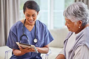 home care nurse looking at a tablet while speaking to a patient