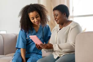 Home care nurse looking at tablet that patient is holding while they are sitting on the couch