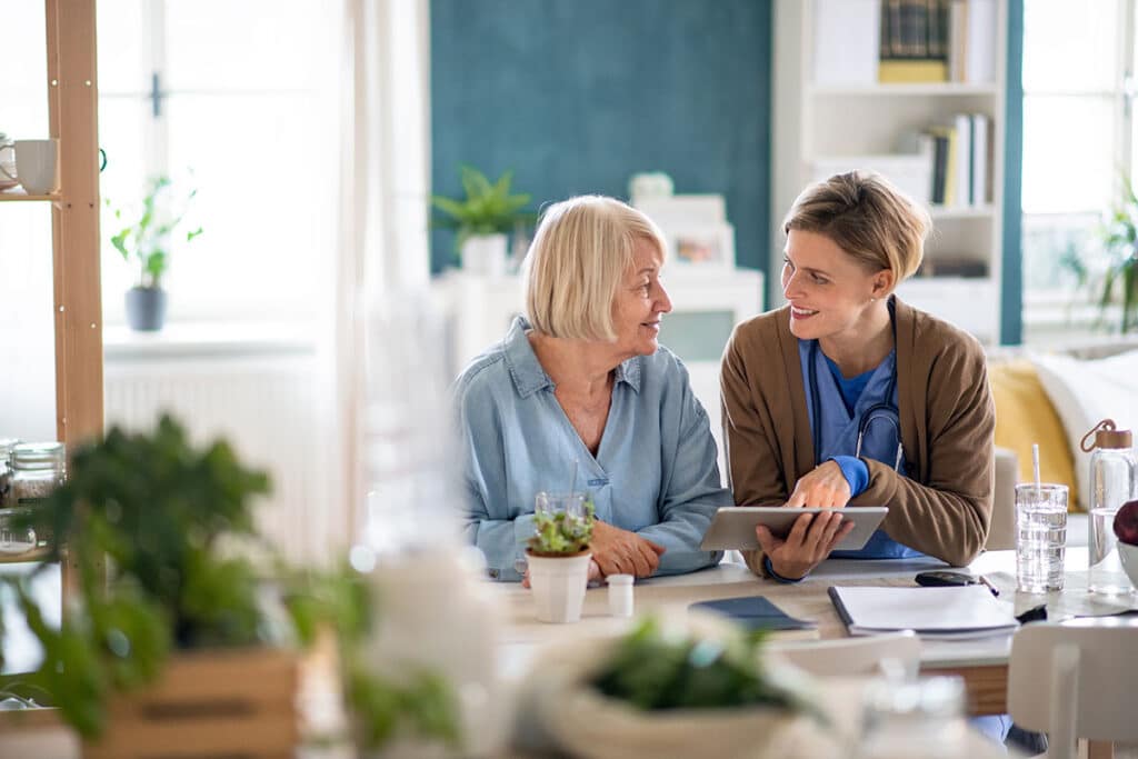 Caregiver or healthcare worker with senior woman patient, using tablet and explaining.