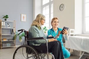 Home care nurse looking at tablet with wheelchair using patient