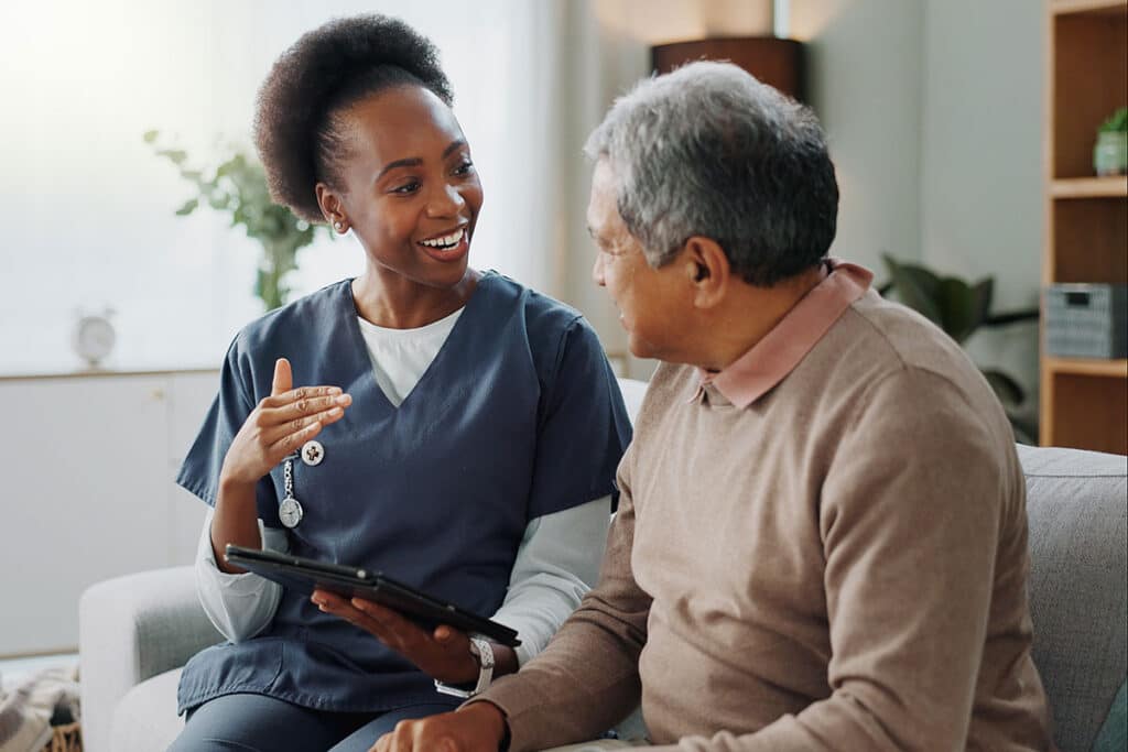 Nurse, senior and consulting with tablet on sofa for healthcare, communication or consultation at home. Woman or medical caregiver talking to elderly male person with technology for advice or help