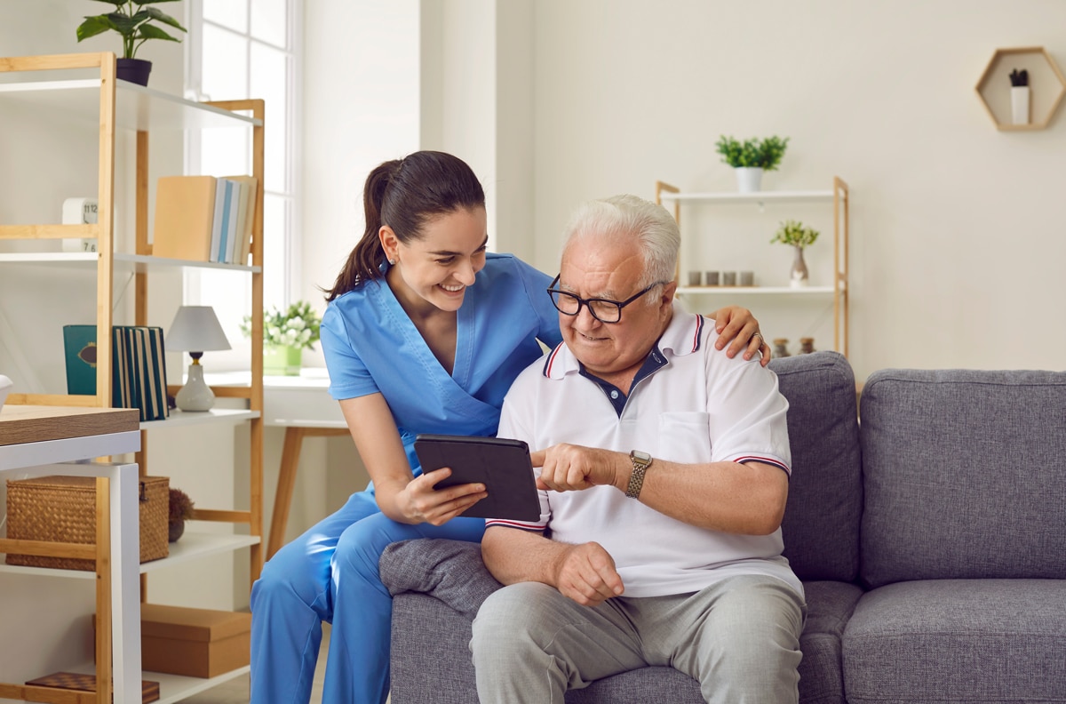 woman-holding-a-tablet-and-smiling-at-an-elderly-man